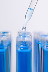 Dripping reagent into test tube with blue liquid on light background, closeup. Laboratory analysis