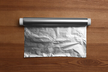 Roll of aluminum foil on wooden table, top view
