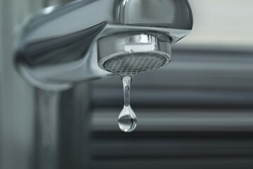 Water drop falling down from tap on blurred background, closeup