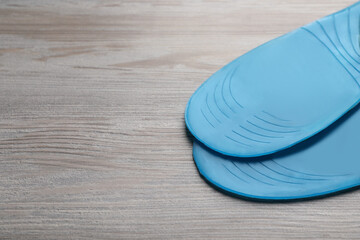 LIght blue orthopedic insoles on wooden background, closeup. Space for text