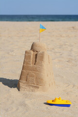Beautiful sand castle with small Ukrainian flag and toy boat on beach near sea