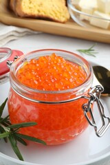 Glass jar of delicious red caviar served with rosemary on plate, closeup