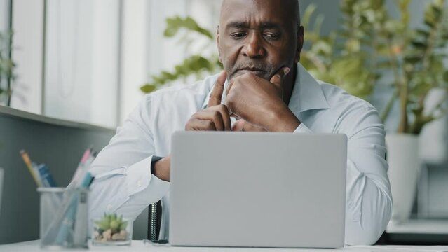 Creative african businessman senior american worker using computer device in office chatting online thinking business solution planning difficult decision pondering strategy come up with idea eureka