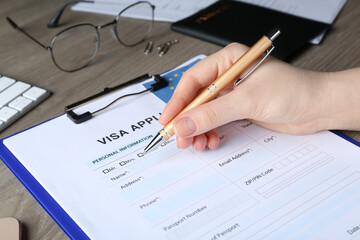 Woman filling visa application form for immigration to European Union at wooden table, closeup