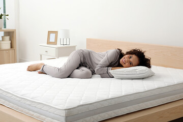 Happy young African American woman on bed with comfortable mattress and pillow at home