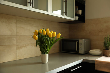 Bouquet of beautiful yellow tulips on countertop in kitchen, space for text