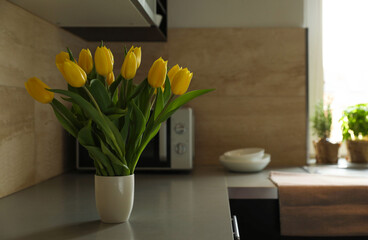 Bouquet of beautiful yellow tulips on countertop in kitchen, space for text