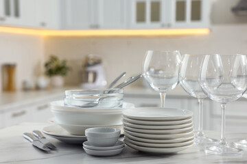 Different clean dishware, cutlery and glasses on white marble table in kitchen