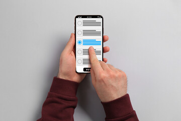 Man voting online via smartphone on light grey background, top view