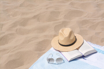 Fototapeta na wymiar Beach towel with straw hat, sunglasses and book on sand. Space for text