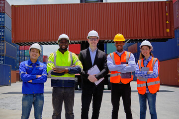 Group of multiracial workers team in safety uniforms, arms crossed and looking at camera at logistics terminal with many stacks of containers, loading shipping goods, cargo transportation industry.