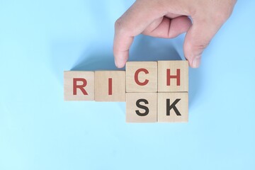 Risk to rich business concept. Hand changing words on wooden blocks in blue background.