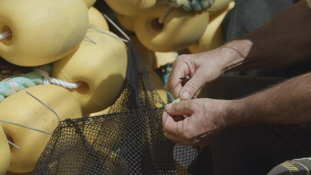 Fisherman is repairing the fishing nets with a big needle. 