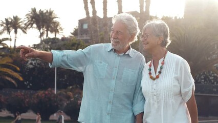 Cute and lovely couple of two old seniors running together holding their hands on the grass of the park. Mature people in love having fun and enjoying summer at the beach.