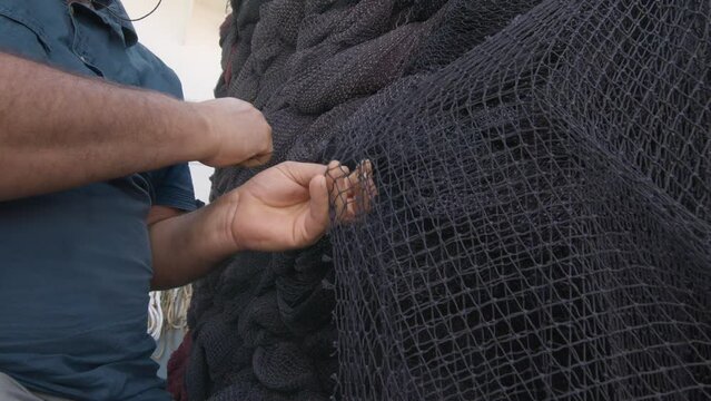 Fisherman is repairing the fishing nets with a big needle. 