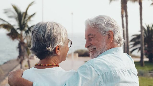 Close up of two cute and happy seniors having fun and enjoying together a sunset day at the beach. Mature couple in love kissing together with the sunset at the background.
