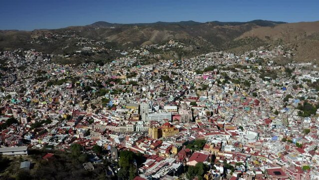 Aerial drone rotating shot of Santa Prisca Parish Church in the center Taxco de Alarcon city in Guerrero state, Mexico surrounded by mountain range at daytime.