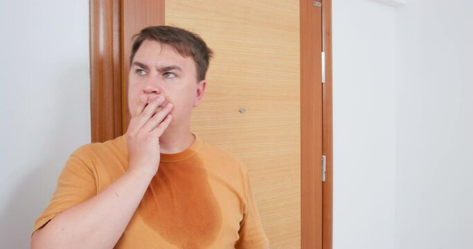 Mature plump man shokingly gazes at thermometer indicator looking very surprised. Man has sweat stain on light brown t-shirt and decides to turn on air conditioner