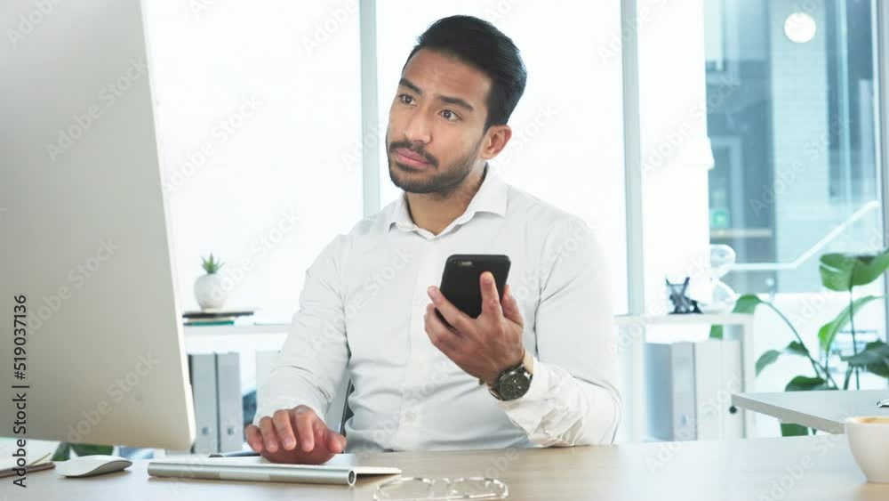 Aufkleber Young business man reading a message on his phone and working on his computer in the office. Handsome corporate professional sending an email and updating the project deadline after receiving a text