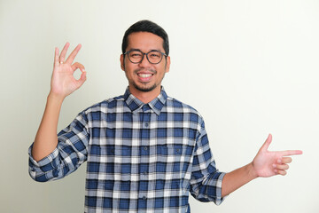 Naklejka premium Adult Asian man smiling happy with left hand pointing to the side