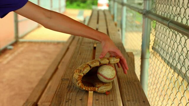 Baseball player picks up ball and glove off dugout bench
