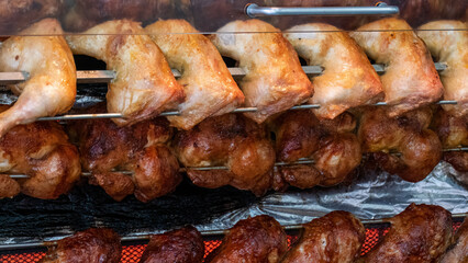 Tasty chicken, chicken legs and turkey drumsticks on a rotisserie in the restaurant