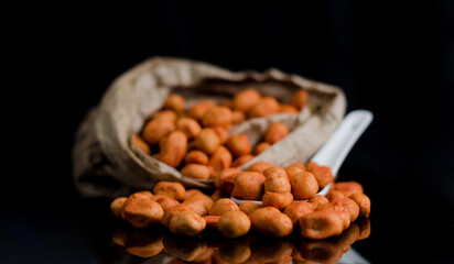 Spicy Japanese peanuts on a table with reflections, on an ecological paper bag. black background