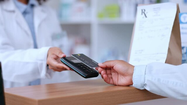 Closeup of customer using contactless payment for medication at a pharmacy. The client takes medicine from medical professional and pays by credit card. Nfc transaction at healthcare chemist.