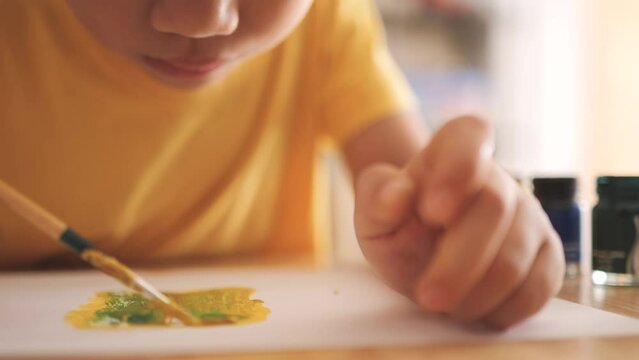 Asian boy drawing and painting a picture with watercolor and brush as a hobby at home.