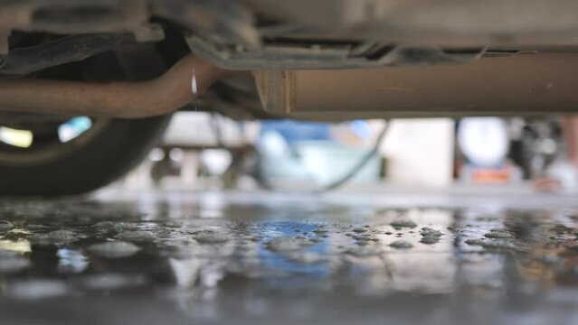 Water pouring under the car from spraying coil cleaner on the AC condenser. A deep cleaning process for air conditioner hygiene.