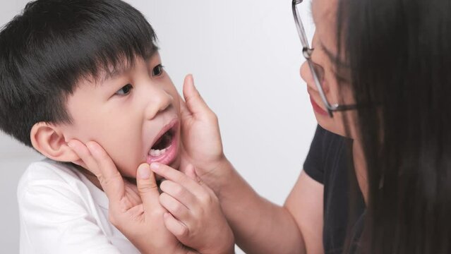 Asian mother checking her son mouth for his dental care. A kid with fallen baby milk teeth and bend tooth.