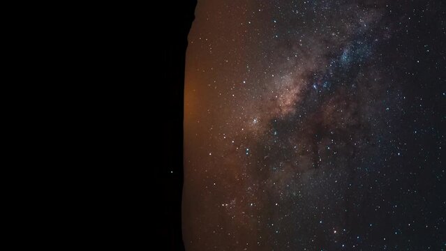 The colorful Milky Way crosses the desert sky above the horizon in silhouette - time lapse vertical orientation
