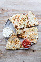 Chicken quesadilla cut in four pieces and served on a silver plate on a wooden table.