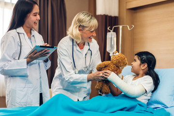Obraz na płótnie Canvas Senior smiling woman doctor service help support discussing and consulting talk to little girl patient give teddy bear and check up information in hospital