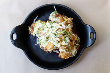 Chicken wings with melted cheese and parsley served in black ceramic bowl
