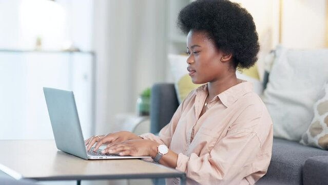 Focused African American female freelancer sits at table at home typing on laptop. Journalist and editor proofreading an article. Concentrating intensely to finish a deadline while working from home.