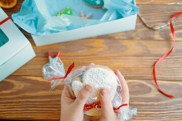Girl's hand holds Christmas gingerbread in form of mitten. Cookies with white icing sugar. Gift box and ribbons on wooden table. Festive atmosphere. New Year light.