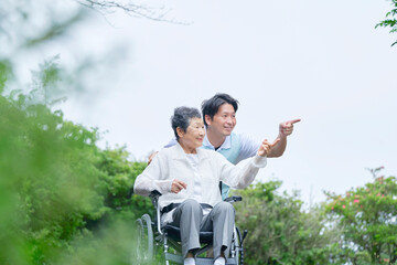屋外で車椅子に乗って介護士と散歩する高齢者女性