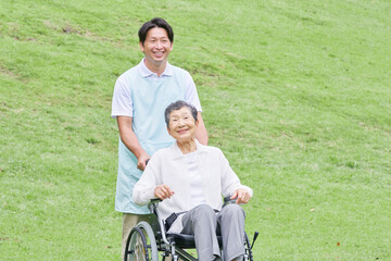 屋外で高齢者女性が乗る車椅子を押す介護士