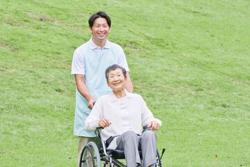 屋外で高齢者女性が乗る車椅子を押す介護士