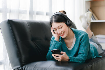 smiling girl relaxing at home She is listening to music using her smartphone and wearing headphones.