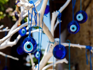 Fototapeta na wymiar The branches of white old tree decorated with the eye-shaped amulets - Nazar boncuk, made of blue glass and believed to protect against the evil eye in Side old town, Turkey.