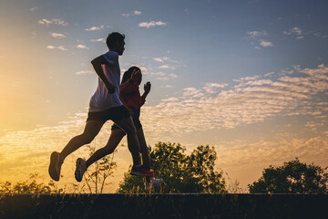 Silhouette of young couple running together on road. Couple, fit runners fitness runners during outdoor workout with sunset background.