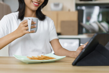 Cozy lifestyle concept, Young woman using tablet while drinking coffee and eating crackers at home