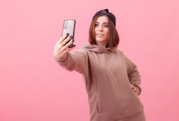Young pretty woman taking selfie on smartphone on pink background