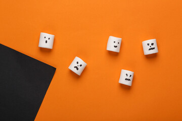 Top view, flat lay halloween layout marshmallows with faces on orange black background. Trick or Treat