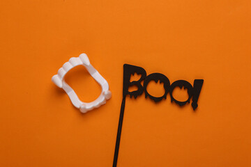 Plastic vampire jaw and the word boo! on a stick on an orange background. Happy Halloween