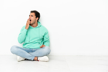 Caucasian handsome man sitting on the floor yawning and covering wide open mouth with hand