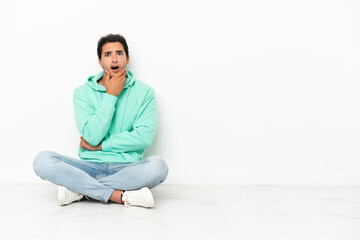 Caucasian handsome man sitting on the floor surprised and shocked while looking right
