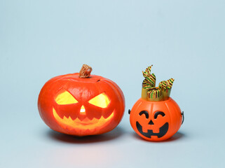 Scary smiling halloween jack lantern pumpkin head with burning candle and halloween candy bucket on blue background